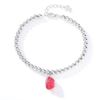 A row of polished sterling silver beads strung into a wrist bracelet, adorned with a translucent bright pink freeform sapphire drop.