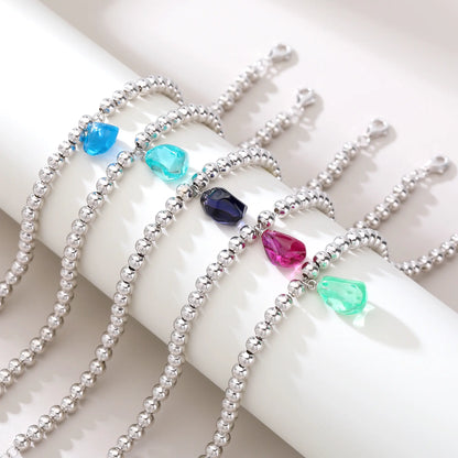 A polished sterling silver spherical bead bracelet featuring a vibrant aqua-blue freeform gemstone charm hanging at the center