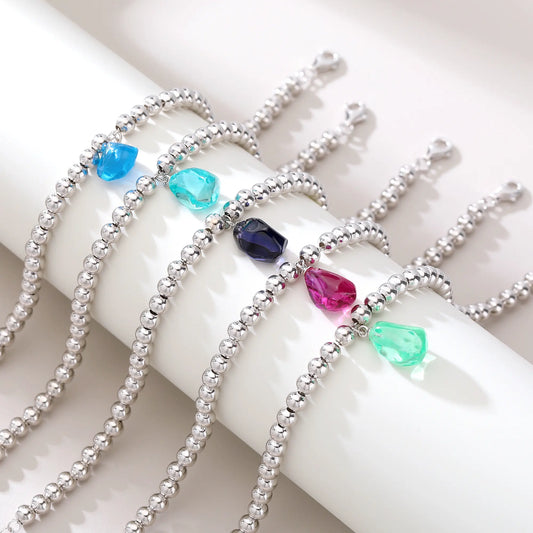A polished sterling silver spherical bead bracelet featuring a vibrant aqua-blue freeform gemstone charm hanging at the center