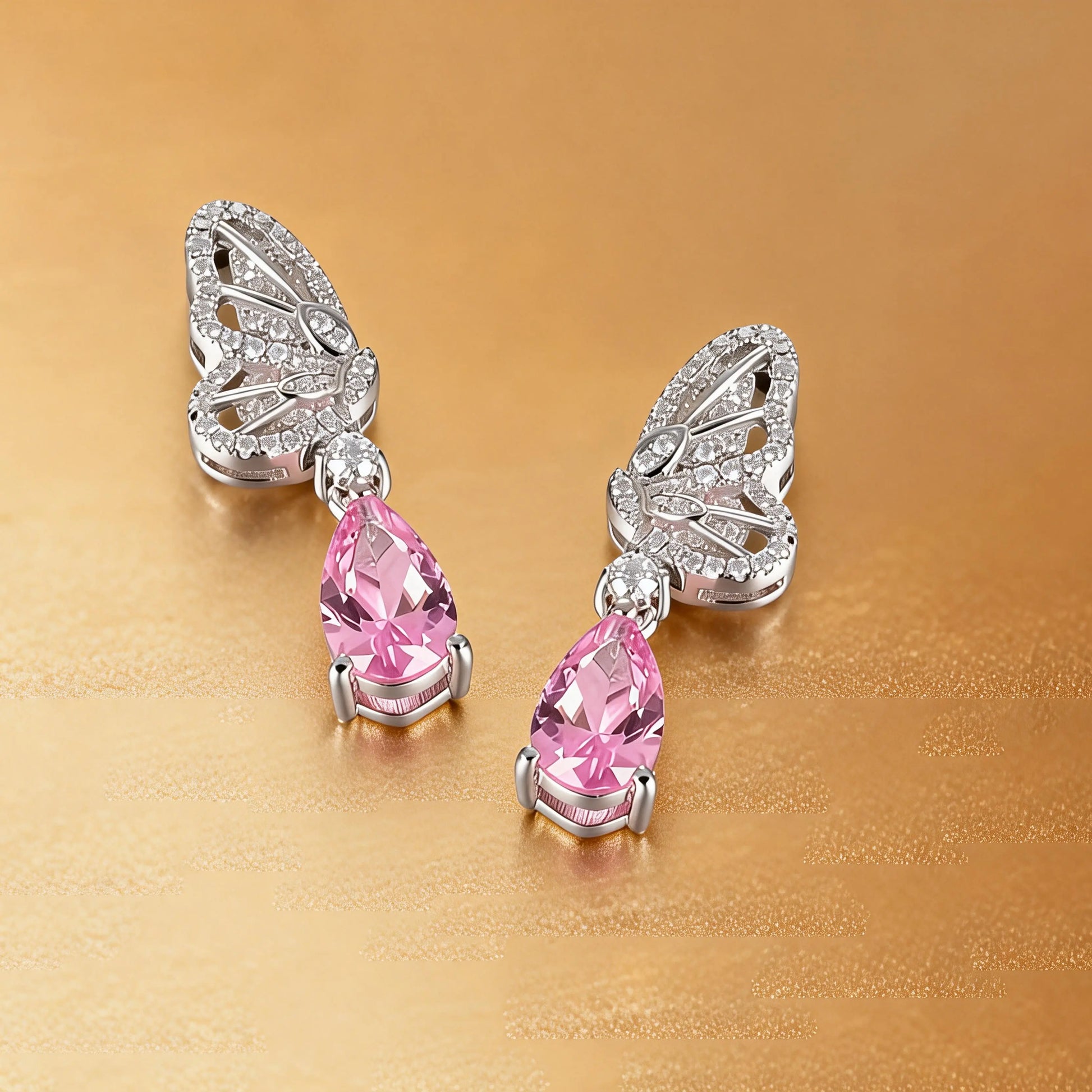 Elegant sterling silver dangle earrings featuring detailed pavé butterfly wings holding vibrant pear-cut pink sapphire stones that catch the light beautifully.