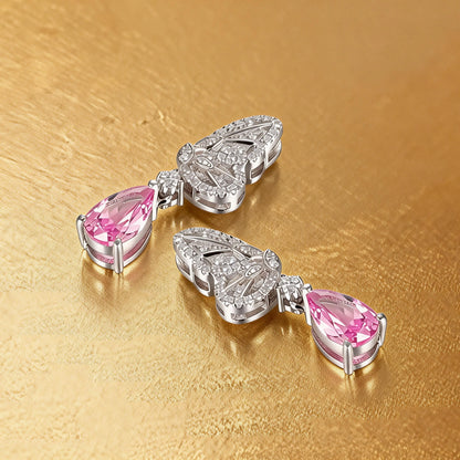 Elegant sterling silver dangle earrings featuring detailed pavé butterfly wings holding vibrant pear-cut pink sapphire stones that catch the light beautifully.