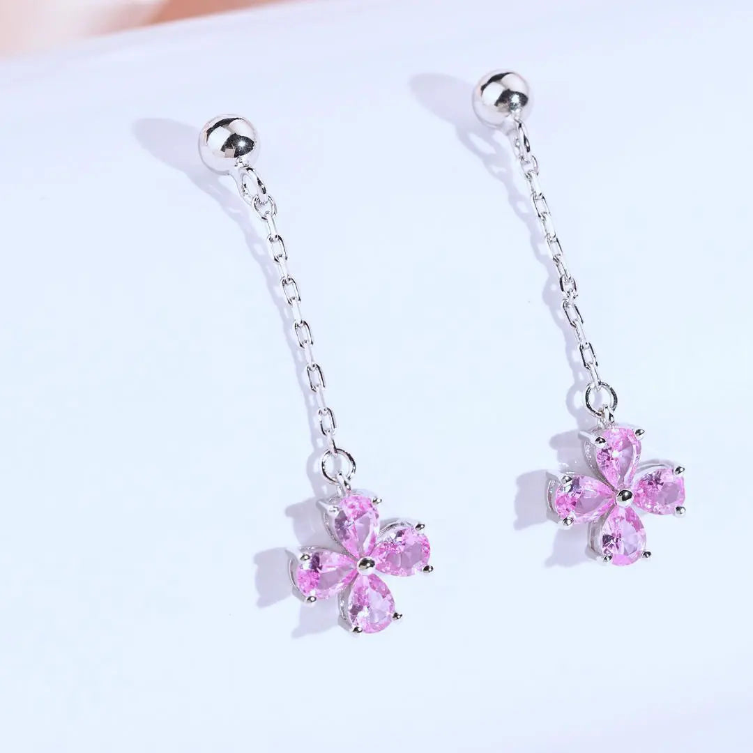A pair of sterling silver drop stud earrings featuring a shimmering four-leaf clover charm made of four pear-cut pink sapphire gemstones, suspended from a delicate silver chain.