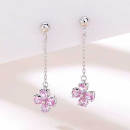 A pair of sterling silver drop stud earrings featuring a shimmering four-leaf clover charm made of four pear-cut pink sapphire gemstones, suspended from a delicate silver chain.