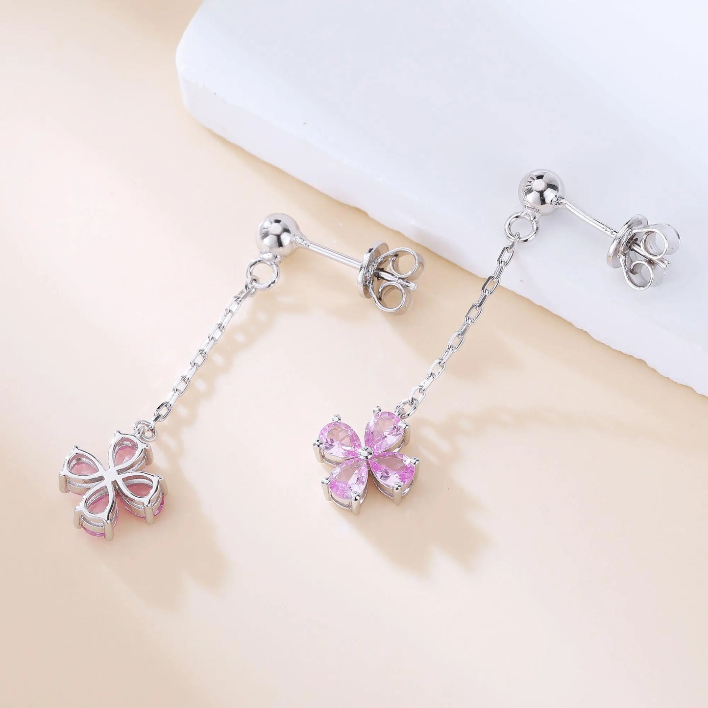 A pair of sterling silver drop stud earrings featuring a shimmering four-leaf clover charm made of four pear-cut pink sapphire gemstones, suspended from a delicate silver chain.