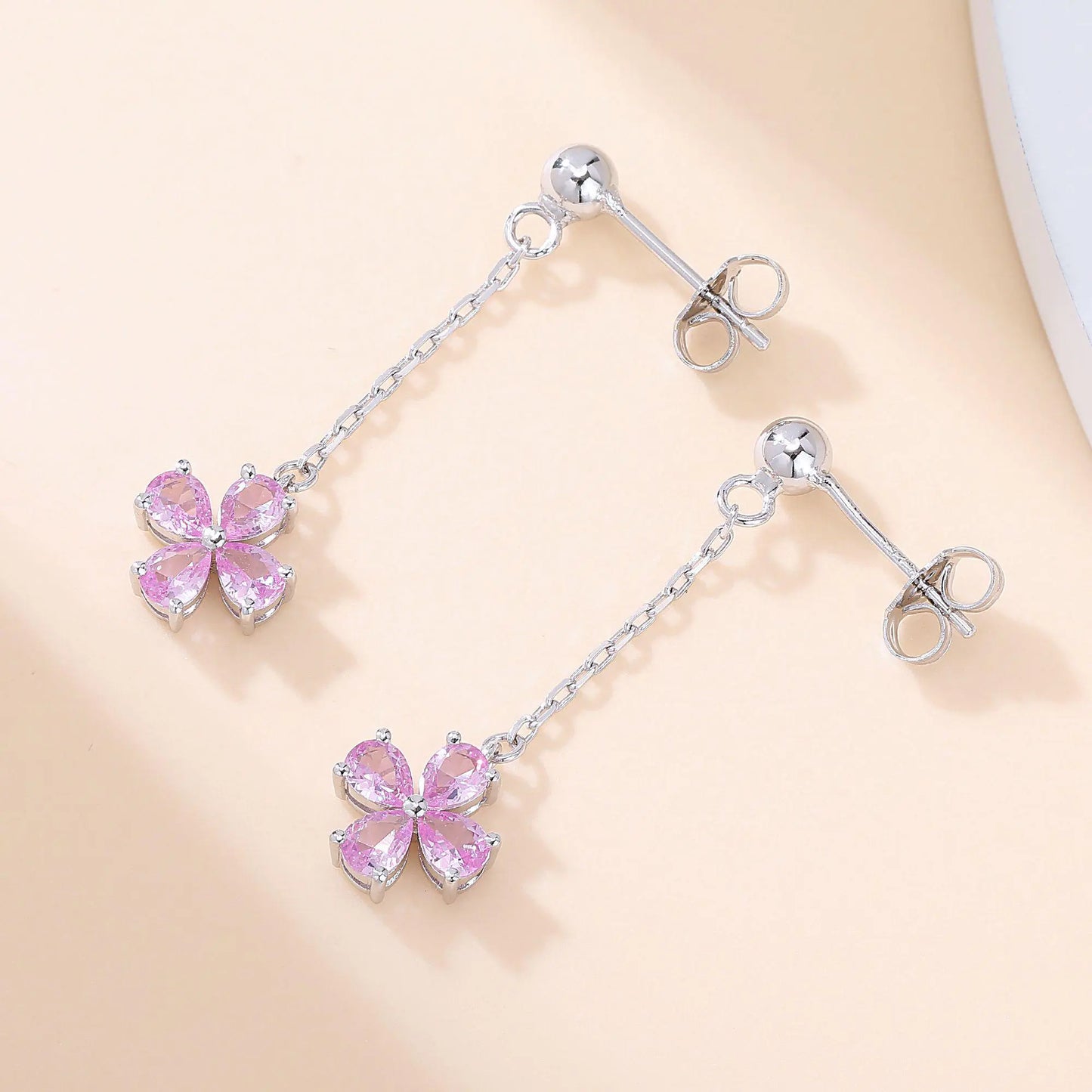 A pair of sterling silver drop stud earrings featuring a shimmering four-leaf clover charm made of four pear-cut pink sapphire gemstones, suspended from a delicate silver chain.