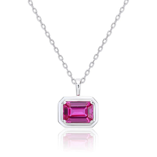 A horizontal emerald cut pink sapphire pendant necklace with a sleek sterling silver bezel setting, showing vibrant pink facets and a reflective white background.
