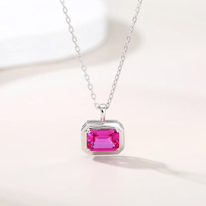 A horizontal emerald cut pink sapphire pendant necklace with a sleek sterling silver bezel setting, showing vibrant pink facets and a reflective white background.