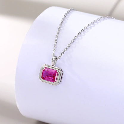 A horizontal emerald cut pink sapphire pendant necklace with a sleek sterling silver bezel setting, showing vibrant pink facets and a reflective white background.