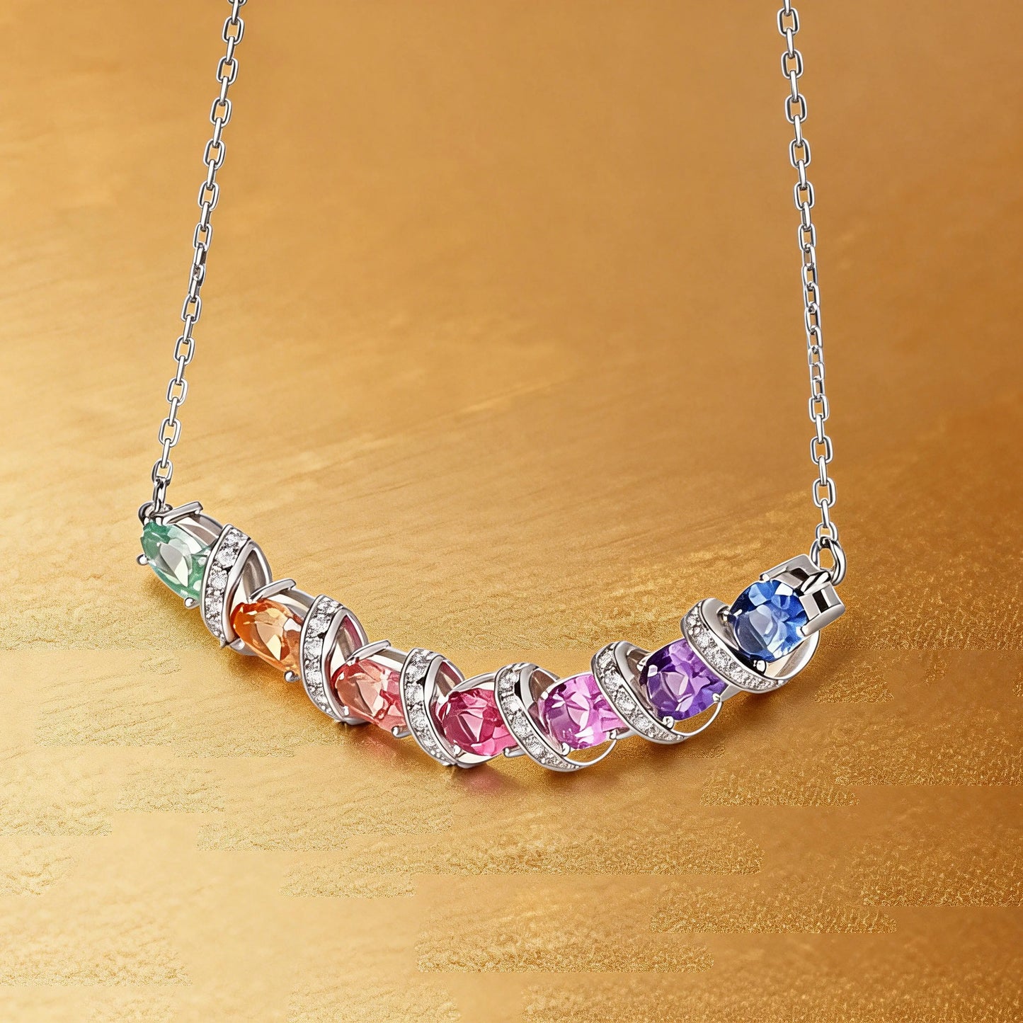 A curved rainbow pendant necklace featuring seven oval cut multi-color sapphires separated by diamond-encrusted silver swirl links, set against a crisp white background.