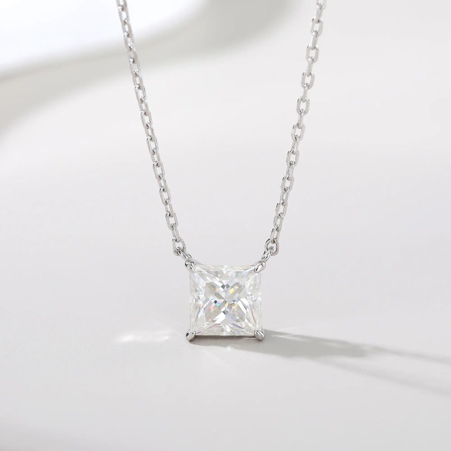 A sparkling princess cut moissanite solitaire pendant necklace in a classic sterling silver four-prong setting, showcasing intense fire and a white reflective surface.