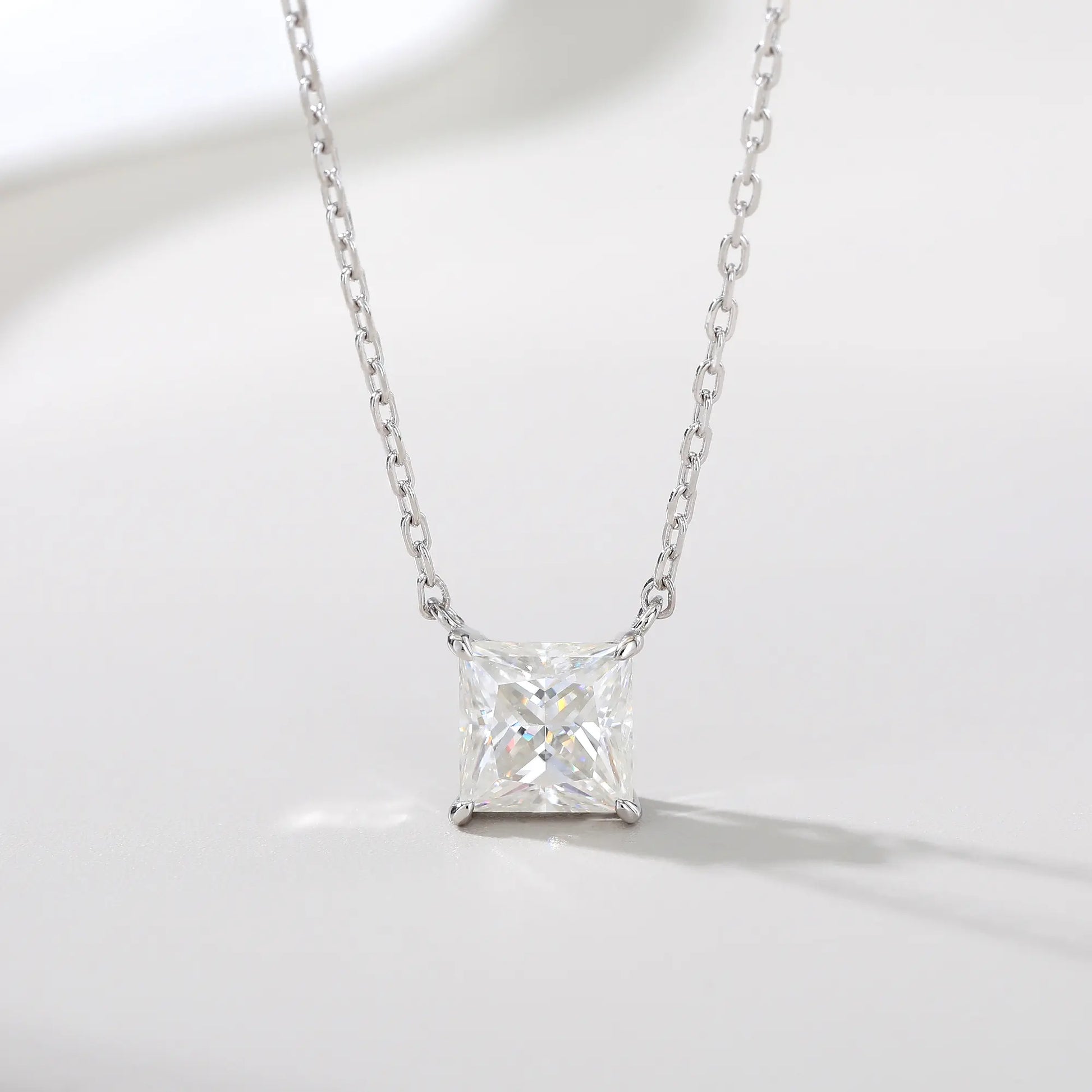 A sparkling princess cut moissanite solitaire pendant necklace in a classic sterling silver four-prong setting, showcasing intense fire and a white reflective surface.