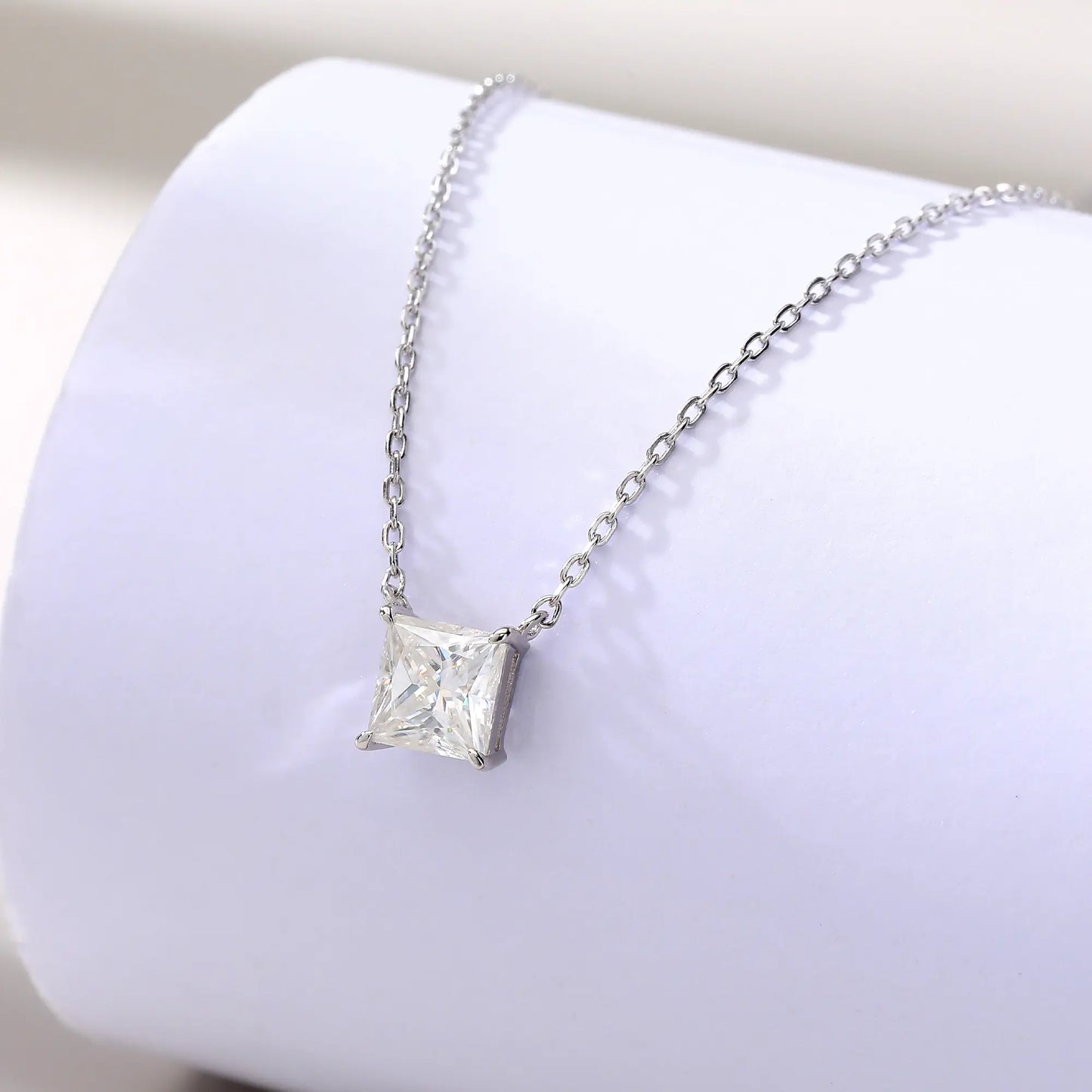 A sparkling princess cut moissanite solitaire pendant necklace in a classic sterling silver four-prong setting, showcasing intense fire and a white reflective surface.