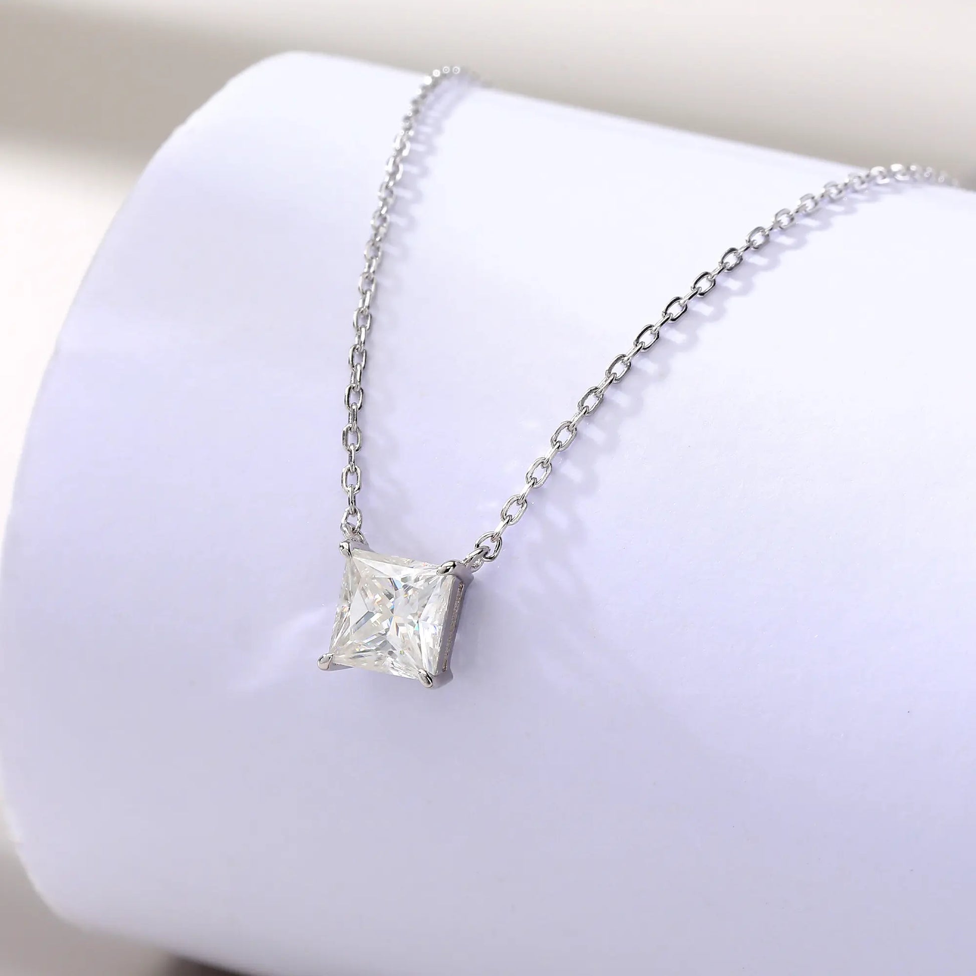 A sparkling princess cut moissanite solitaire pendant necklace in a classic sterling silver four-prong setting, showcasing intense fire and a white reflective surface.