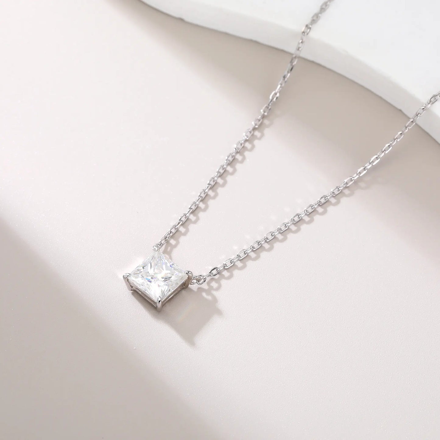 A sparkling princess cut moissanite solitaire pendant necklace in a classic sterling silver four-prong setting, showcasing intense fire and a white reflective surface.