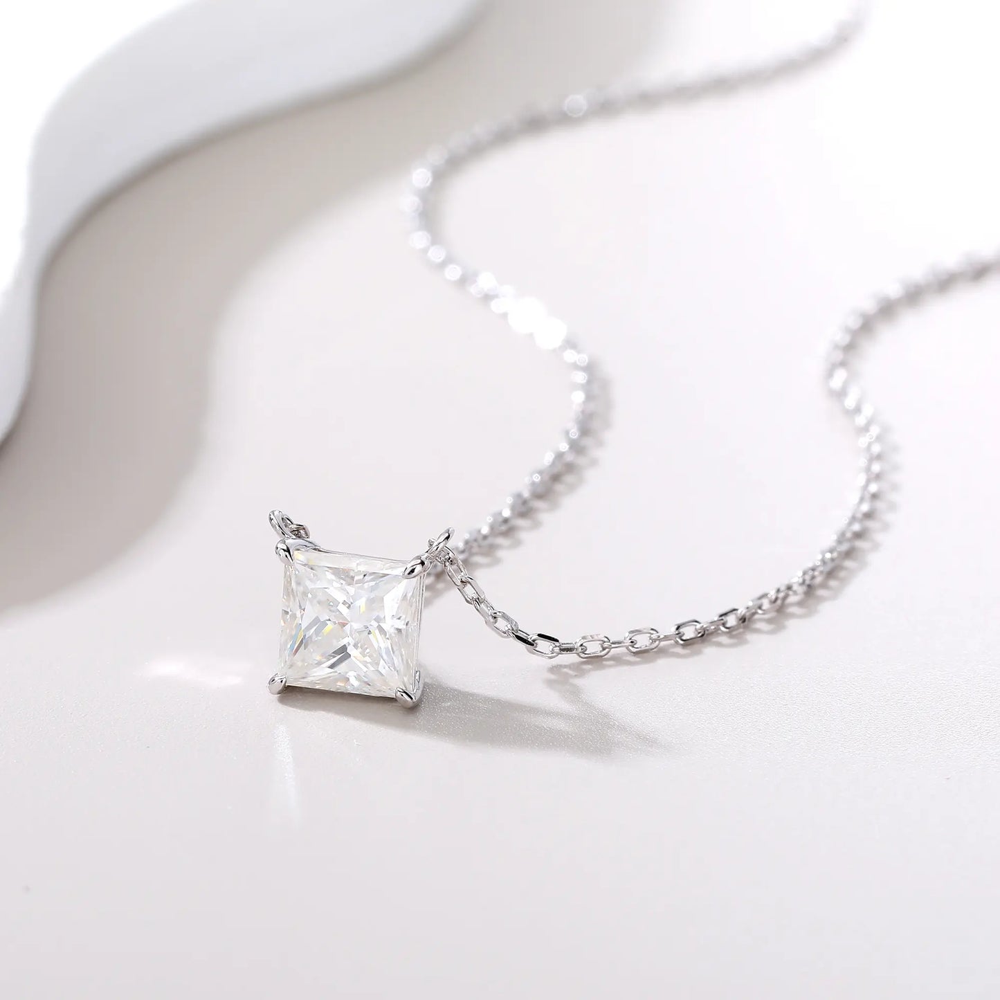 A sparkling princess cut moissanite solitaire pendant necklace in a classic sterling silver four-prong setting, showcasing intense fire and a white reflective surface.