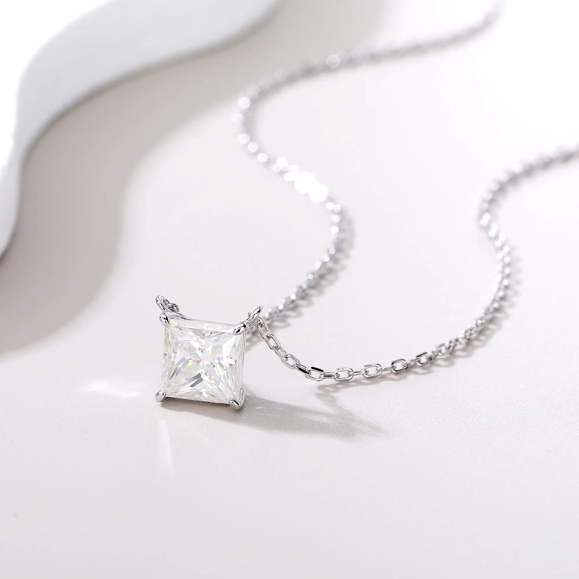 A sparkling princess cut moissanite solitaire pendant necklace in a classic sterling silver four-prong setting, showcasing intense fire and a white reflective surface.