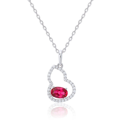 An openwork gourd pendant necklace paved with sparkling cz stones, featuring a horizontally set oval cut ruby at the base, resting on a white reflective surface.