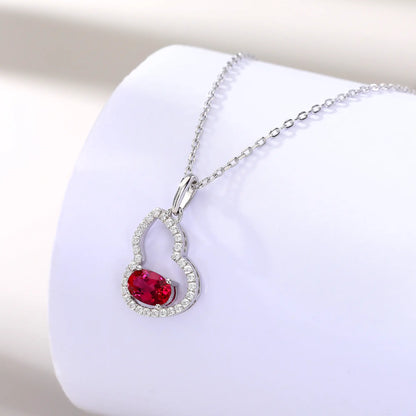 An openwork gourd pendant necklace paved with sparkling cz stones, featuring a horizontally set oval cut ruby at the base, resting on a white reflective surface.