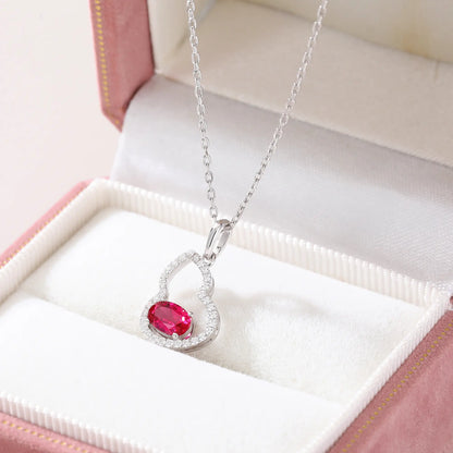 An openwork gourd pendant necklace paved with sparkling cz stones, featuring a horizontally set oval cut ruby at the base, resting on a white reflective surface.