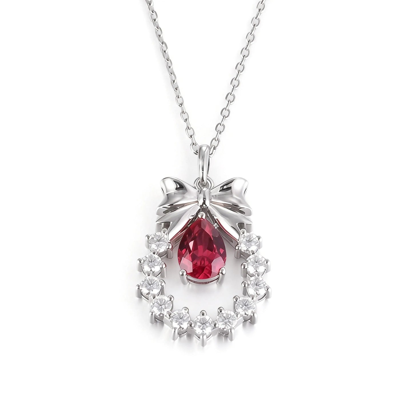 A delicate sterling silver pendant necklace featuring an elegant metal bow tied above a sparkling halo wreath, centering a vibrant pear-cut red ruby teardrop that catches the light.