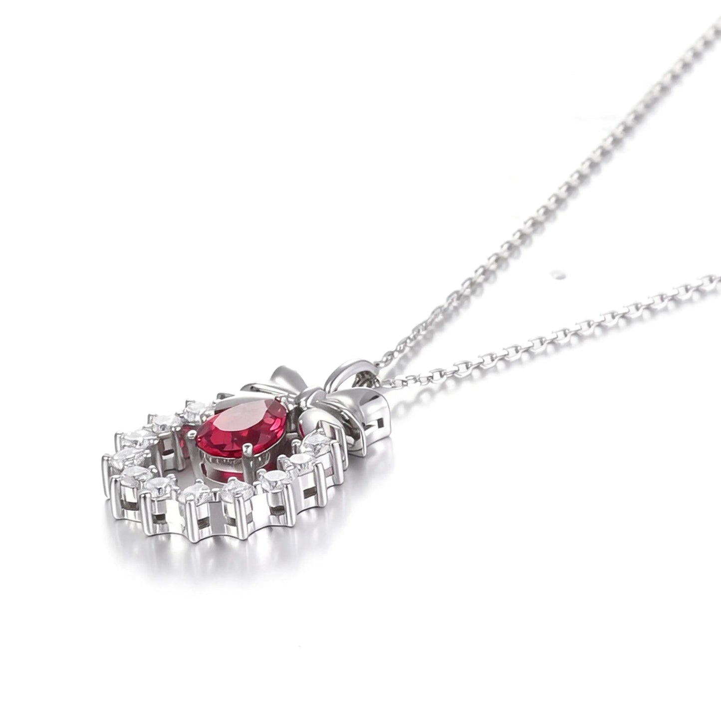 A delicate sterling silver pendant necklace featuring an elegant metal bow tied above a sparkling halo wreath, centering a vibrant pear-cut red ruby teardrop that catches the light.
