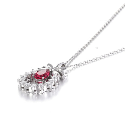 A delicate sterling silver pendant necklace featuring an elegant metal bow tied above a sparkling halo wreath, centering a vibrant pear-cut red ruby teardrop that catches the light.