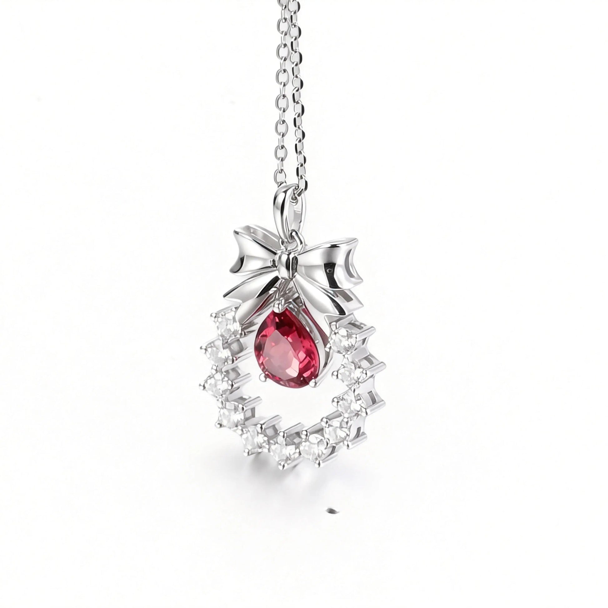 A delicate sterling silver pendant necklace featuring an elegant metal bow tied above a sparkling halo wreath, centering a vibrant pear-cut red ruby teardrop that catches the light.