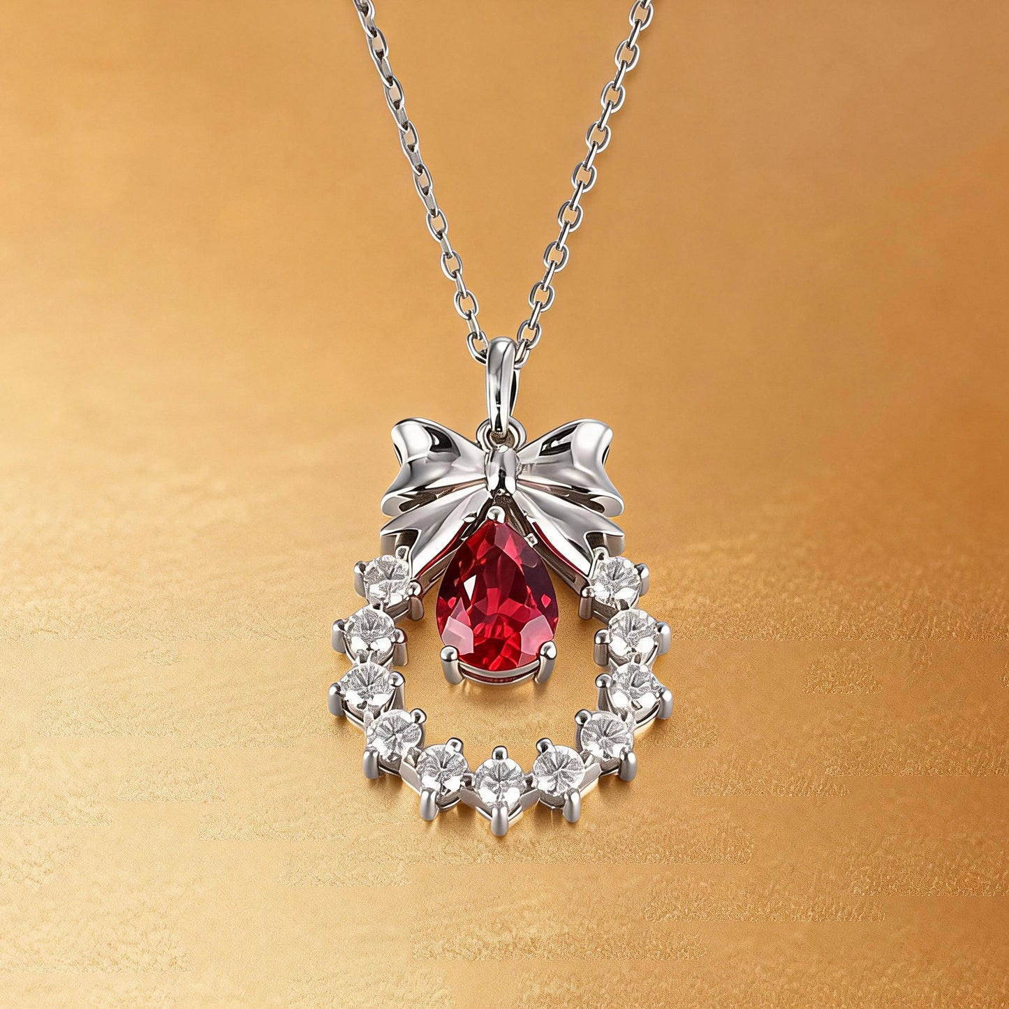 A delicate sterling silver pendant necklace featuring an elegant metal bow tied above a sparkling halo wreath, centering a vibrant pear-cut red ruby teardrop that catches the light.