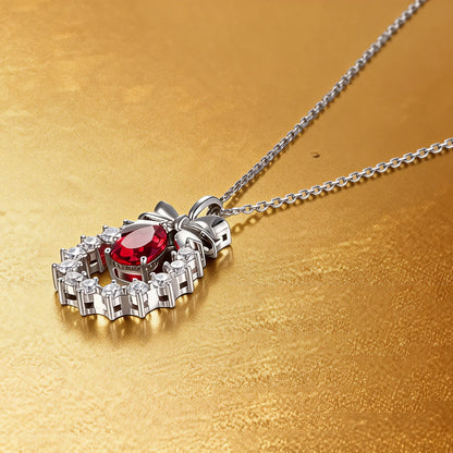 A delicate sterling silver pendant necklace featuring an elegant metal bow tied above a sparkling halo wreath, centering a vibrant pear-cut red ruby teardrop that catches the light.