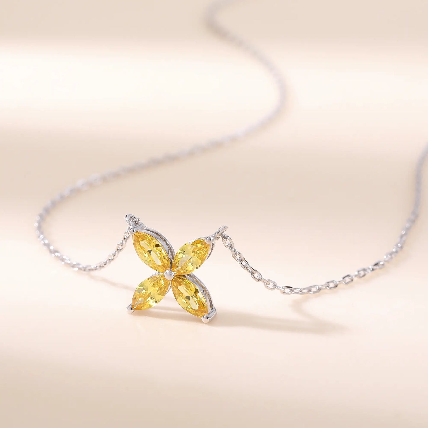 A sterling silver chain necklace featuring a classic minimalist four-leaf clover flower pendant crafted with four brilliant marquise-cut yellow moissanite gemstones.