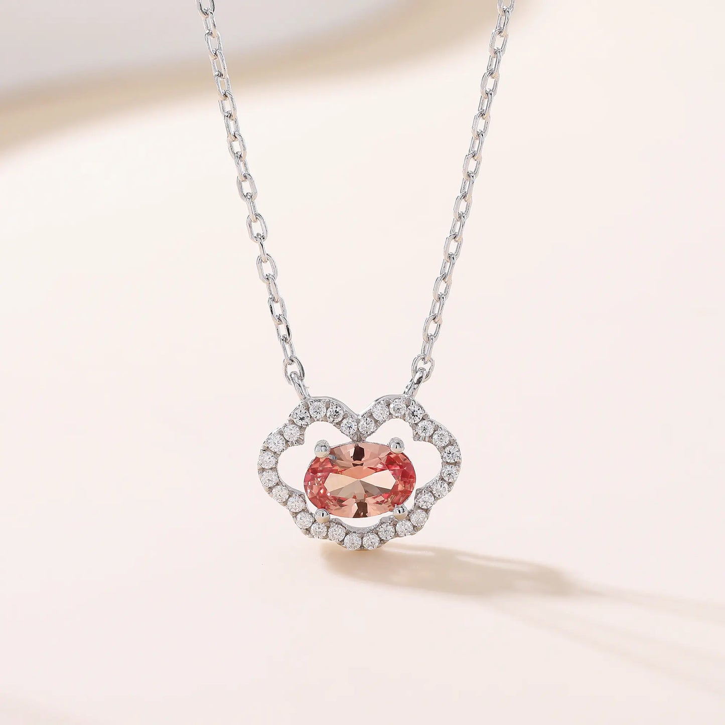 A sterling silver chain necklace featuring a traditional Chinese auspicious Ruyi cloud pendant, encrusted with pavé accents and centered with an oval-cut padparadscha sapphire.