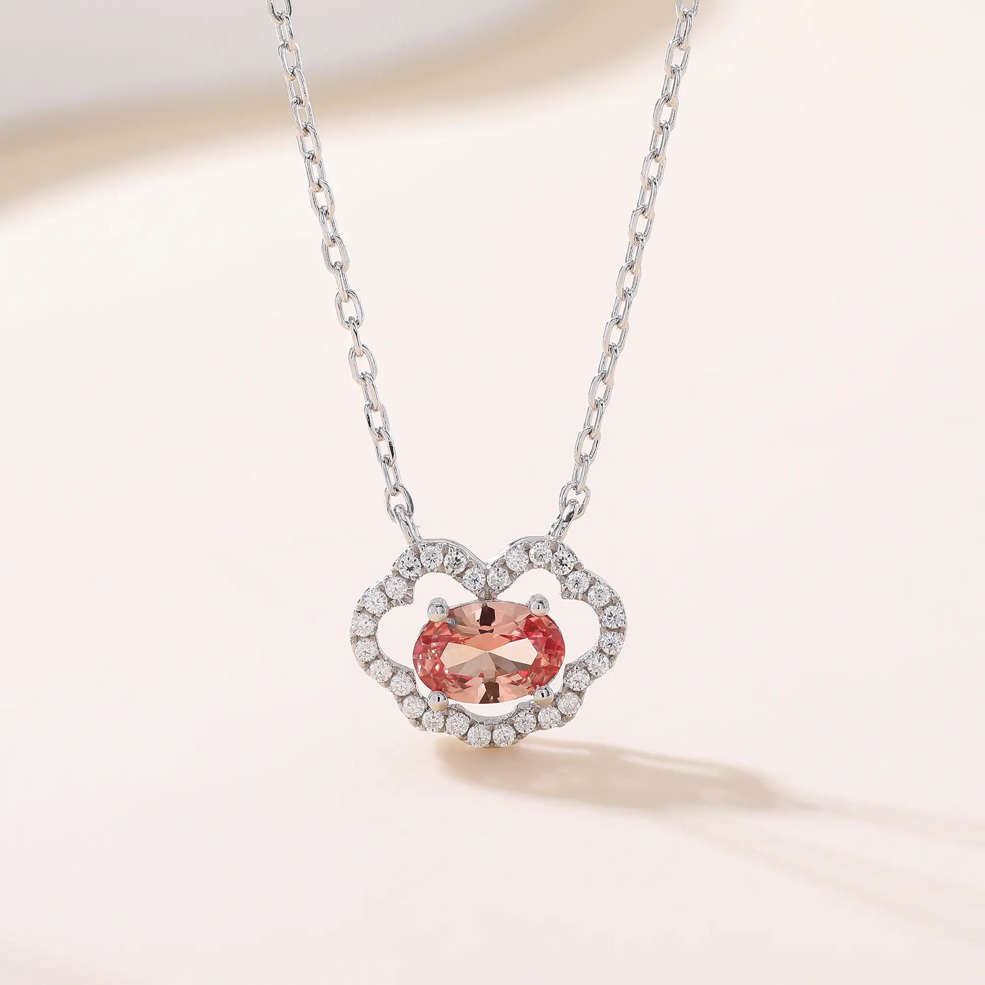 A sterling silver chain necklace featuring a traditional Chinese auspicious Ruyi cloud pendant, encrusted with pavé accents and centered with an oval-cut padparadscha sapphire.