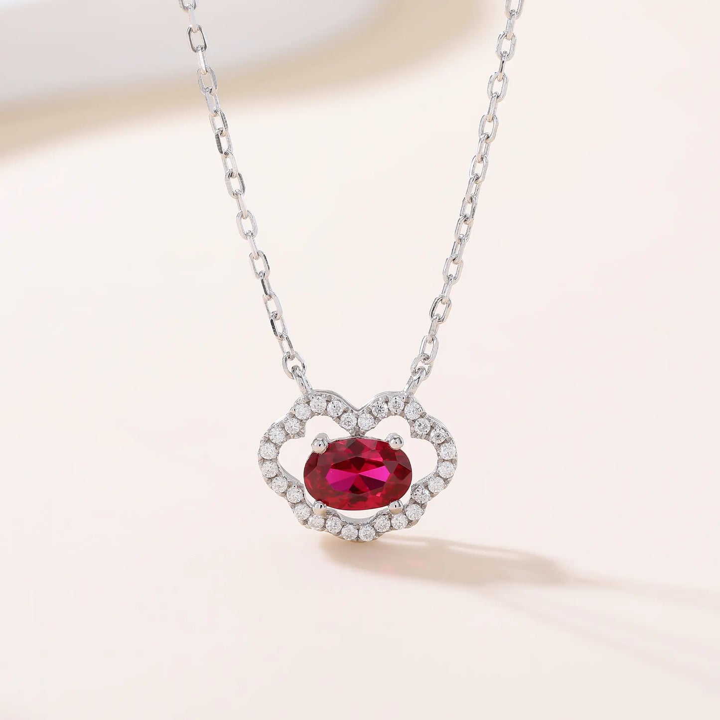A sterling silver chain necklace featuring a traditional Chinese auspicious Ruyi cloud pendant, encrusted with pavé accents and centered with a vibrant oval-cut red ruby gemstone.