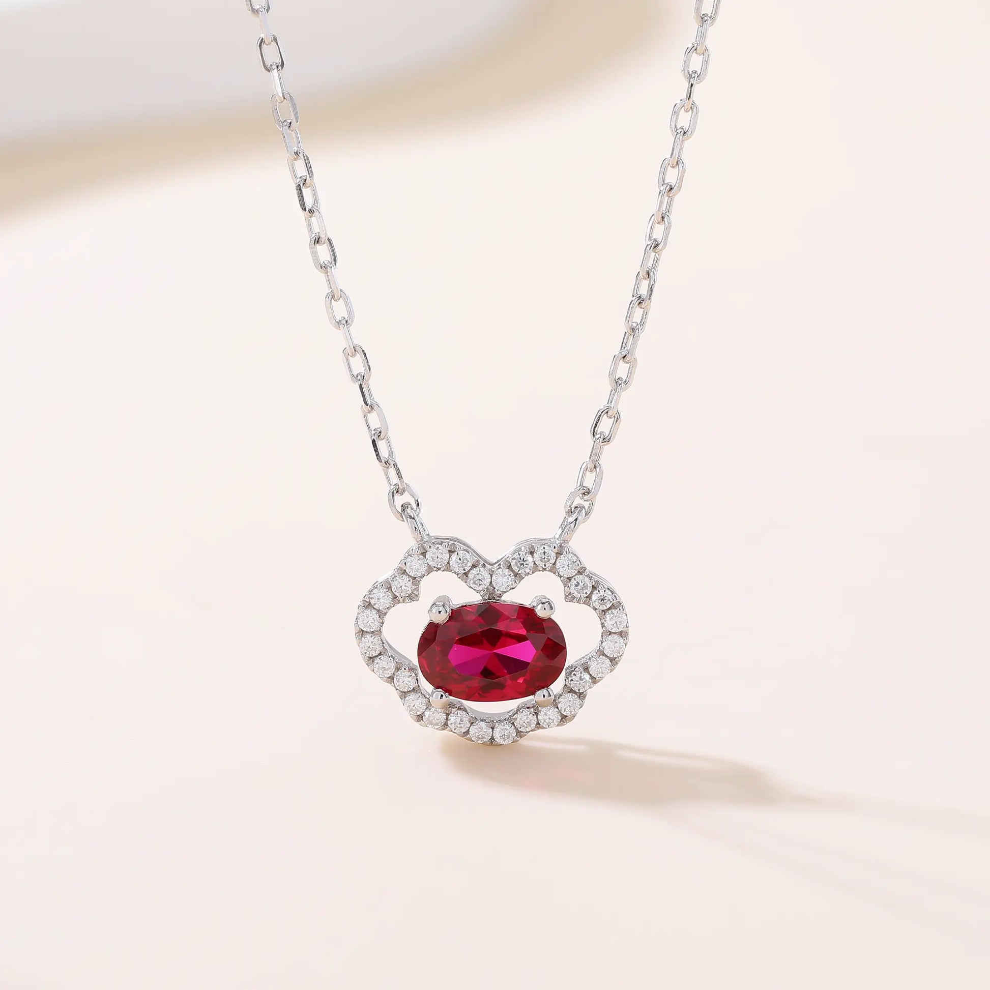 A sterling silver chain necklace featuring a traditional Chinese auspicious Ruyi cloud pendant, encrusted with pavé accents and centered with a vibrant oval-cut red ruby gemstone.