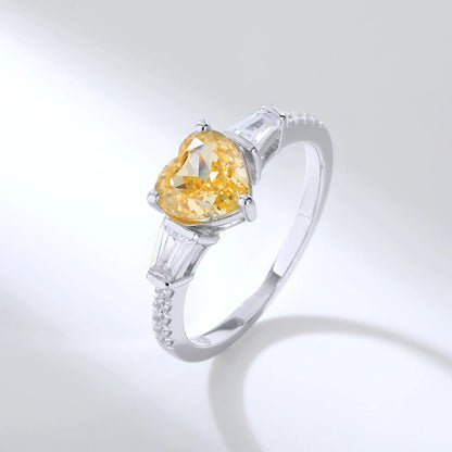 S925 sterling silver three-stone ring featuring a heart-cut yellow sapphire center stone flanked by tapered baguette cut moissanites on a pavé band.