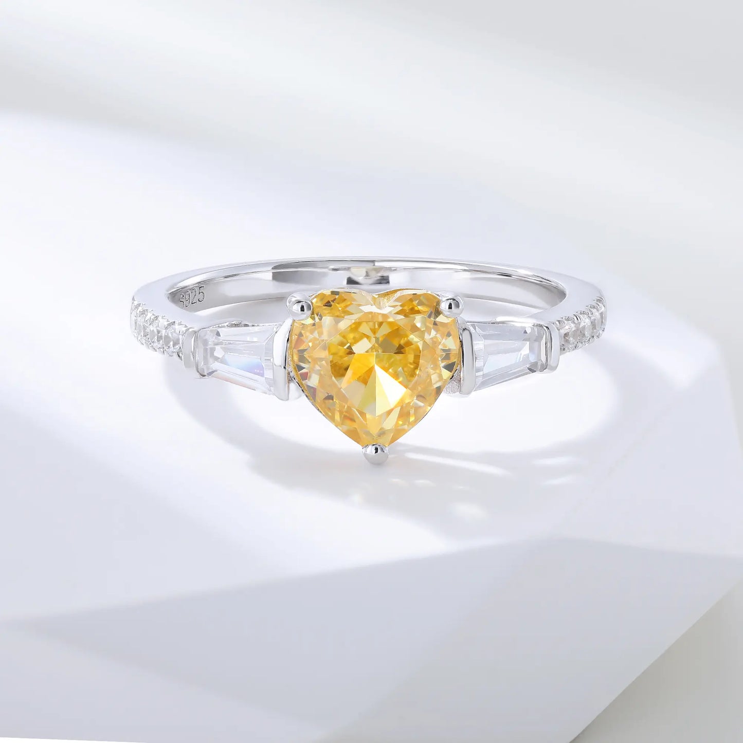 S925 sterling silver three-stone ring featuring a heart-cut yellow sapphire center stone flanked by tapered baguette cut moissanites on a pavé band.