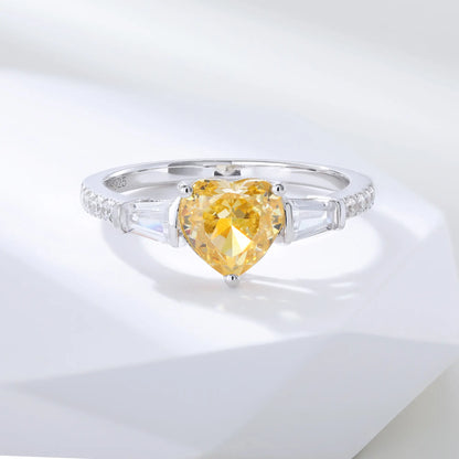 S925 sterling silver three-stone ring featuring a heart-cut yellow sapphire center stone flanked by tapered baguette cut moissanites on a pavé band.