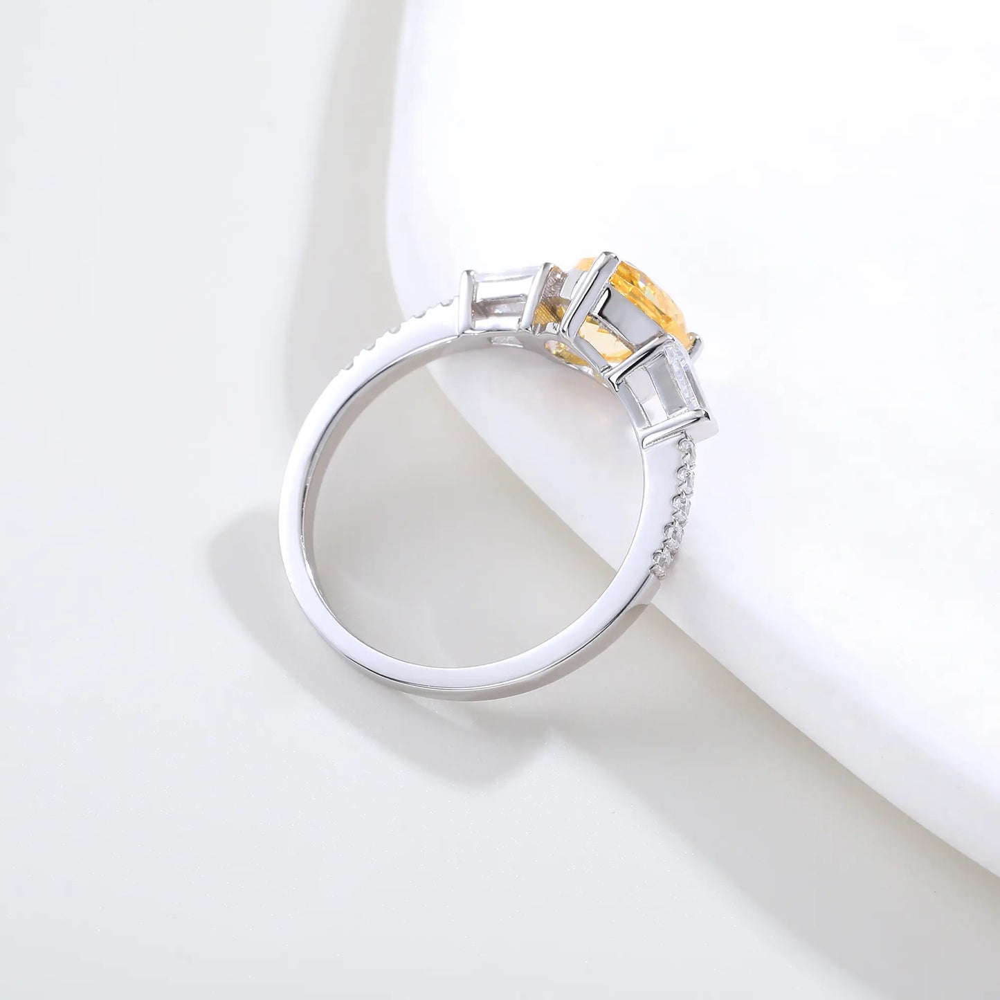 S925 sterling silver three-stone ring featuring a heart-cut yellow sapphire center stone flanked by tapered baguette cut moissanites on a pavé band.
