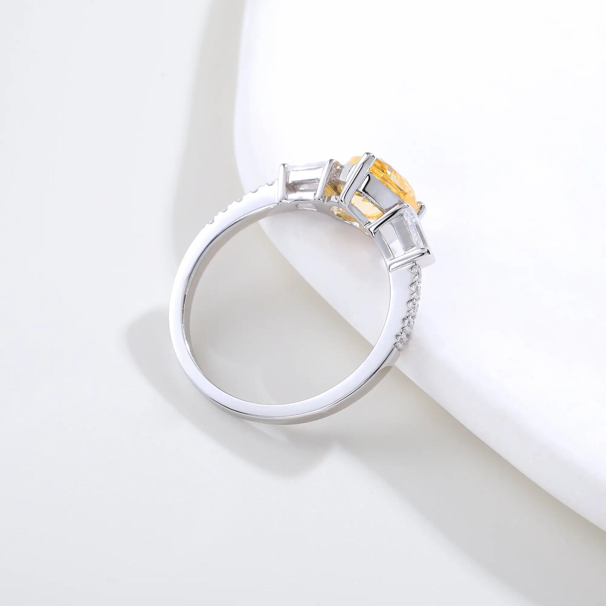 S925 sterling silver three-stone ring featuring a heart-cut yellow sapphire center stone flanked by tapered baguette cut moissanites on a pavé band.