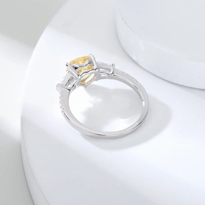 S925 sterling silver three-stone ring featuring a heart-cut yellow sapphire center stone flanked by tapered baguette cut moissanites on a pavé band.