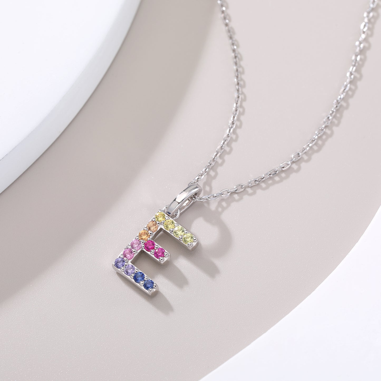 Dainty sterling silver cable chain necklace showcasing a block letter E charm encrusted with a rainbow spectrum of lab-created colored sapphires.