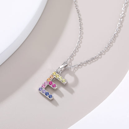 Dainty sterling silver cable chain necklace showcasing a block letter E charm encrusted with a rainbow spectrum of lab-created colored sapphires.