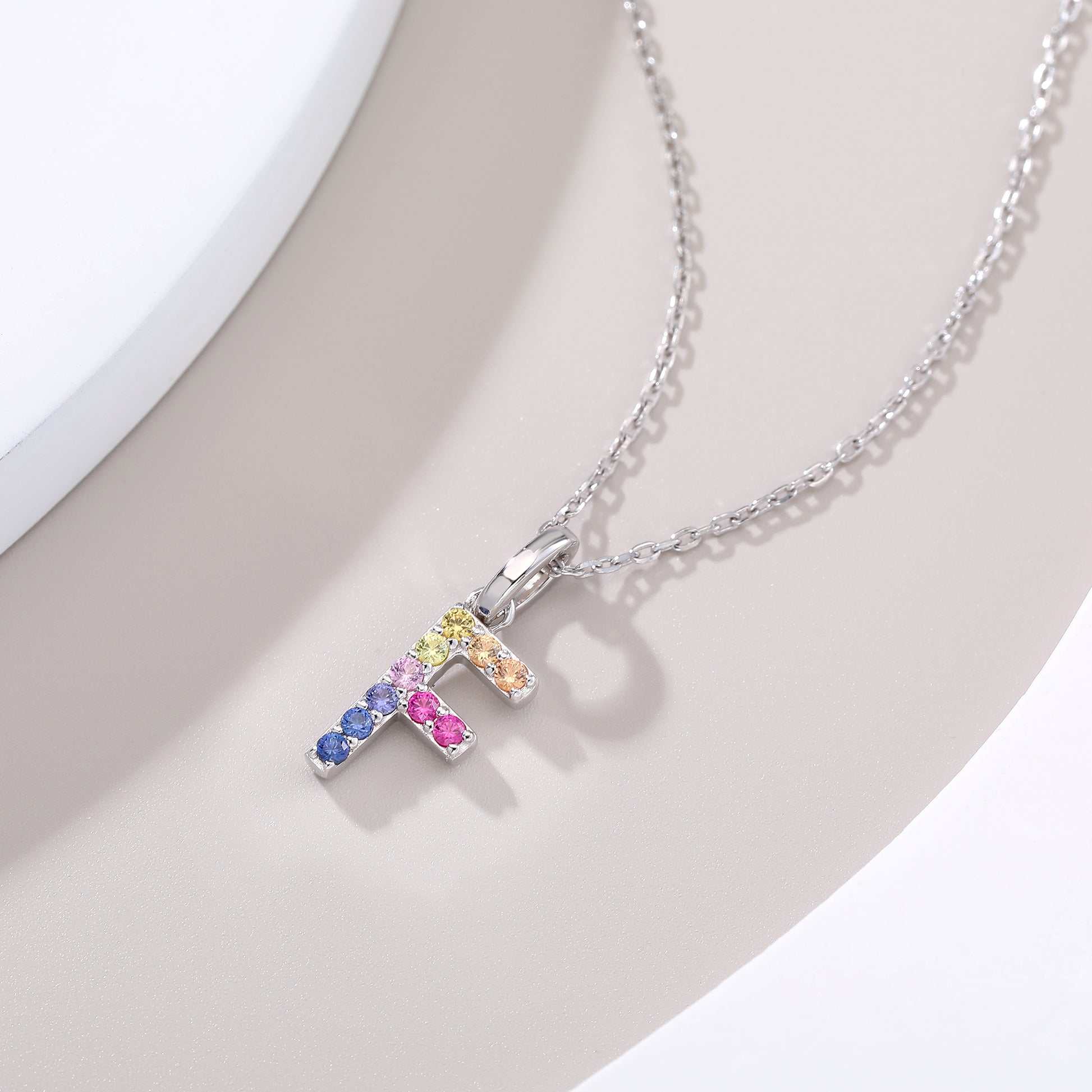 A silver letter F alphabet charm beautifully set with a shifting rainbow palette of round lab-grown sapphires on a classic link chain.
