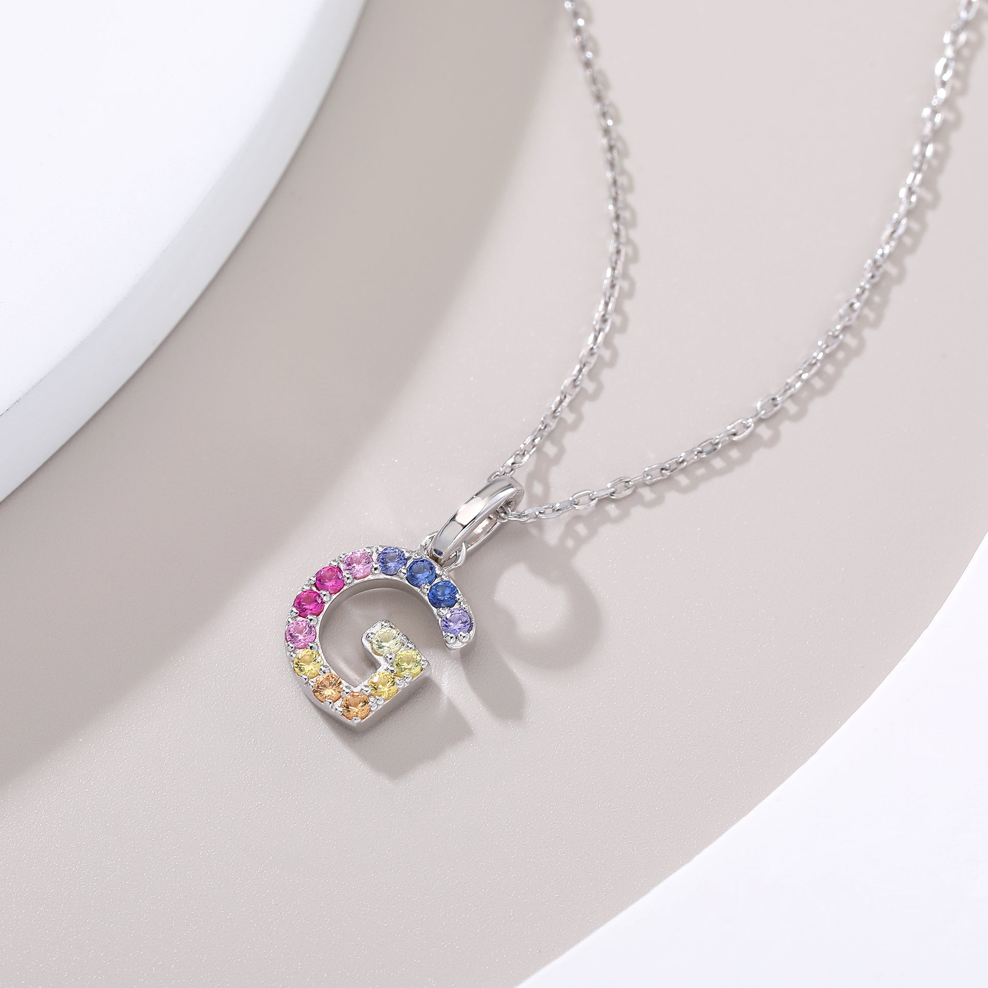 A delicate sterling silver necklace displaying a capital letter G charm micro-pave set with a shifting rainbow curve of lab-grown multi-color sapphires.
