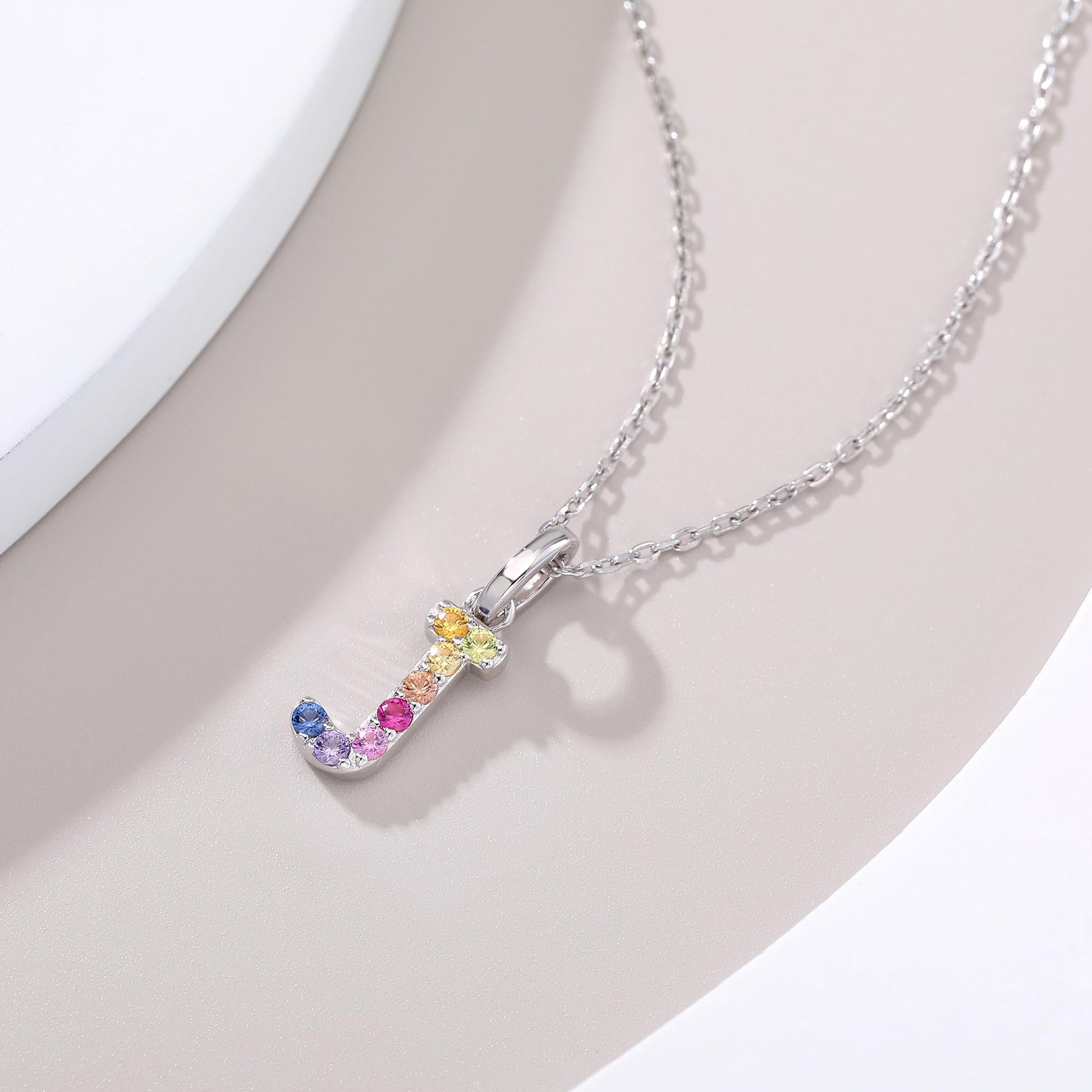 A graceful sterling silver cable chain necklace presenting a capital letter J charm set with a fluid rainbow arc of multi-color lab sapphires.