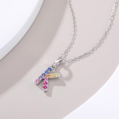 A solid sterling silver necklace displaying a sharp letter K pendant prong-set with a striking multi-color rainbow gradient of brilliant lab sapphires.