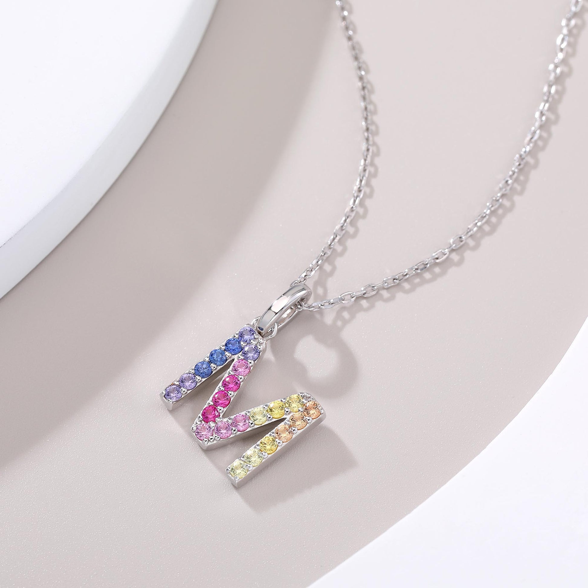 A classic sterling silver initial necklace showcasing an uppercase letter M pendant encrusted with a sweeping zig-zag rainbow gradient of brilliant multi-color lab sapphires.