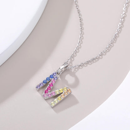 A classic sterling silver initial necklace showcasing an uppercase letter M pendant encrusted with a sweeping zig-zag rainbow gradient of brilliant multi-color lab sapphires.