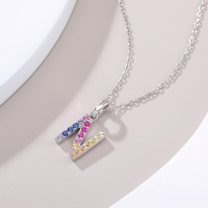 A delicate sterling silver chain necklace holding an uppercase letter N pendant intricately hand-set with a fluid rainbow gradient of multi-color lab sapphires.