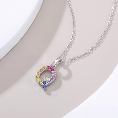 A solid sterling silver necklace displaying an uppercase letter Q monogram pendant, highlighted by a playful tail and handset with a continuous rainbow gradient of round lab sapphires.